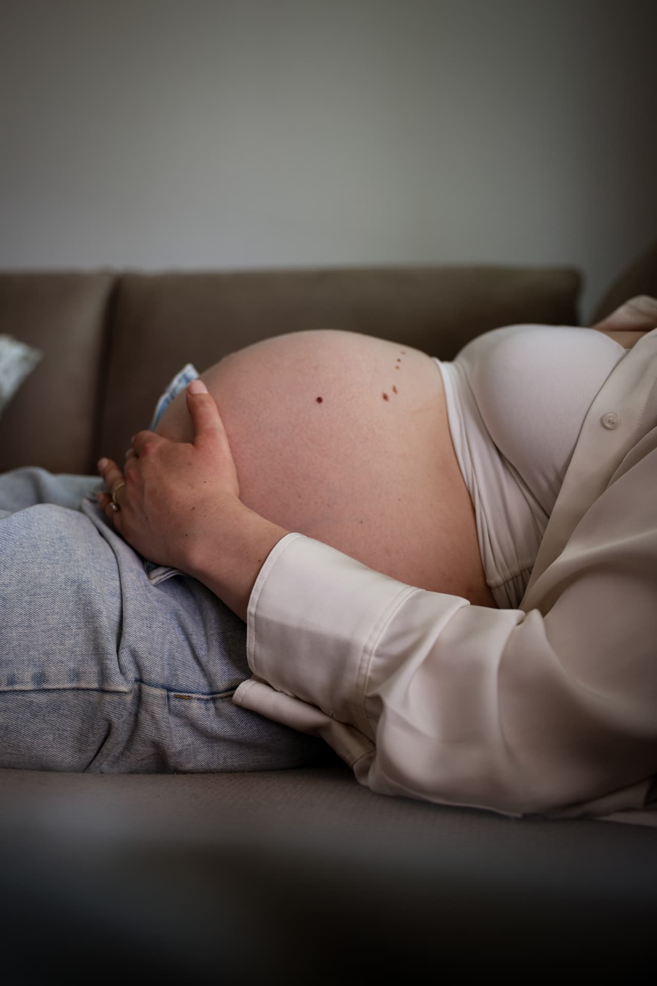 Schwangere liegt seitlich auf einem Sofa und umarmt ihren Babybauch