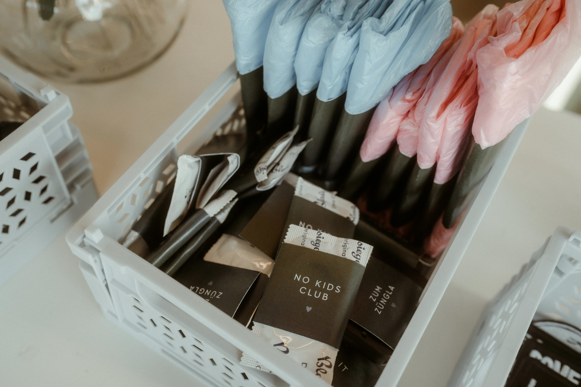 Gefüllte Kunststoffkiste mit NO KIDS CLUB-Tütchen und in Hellblau und Rosa verpackten Giveaways