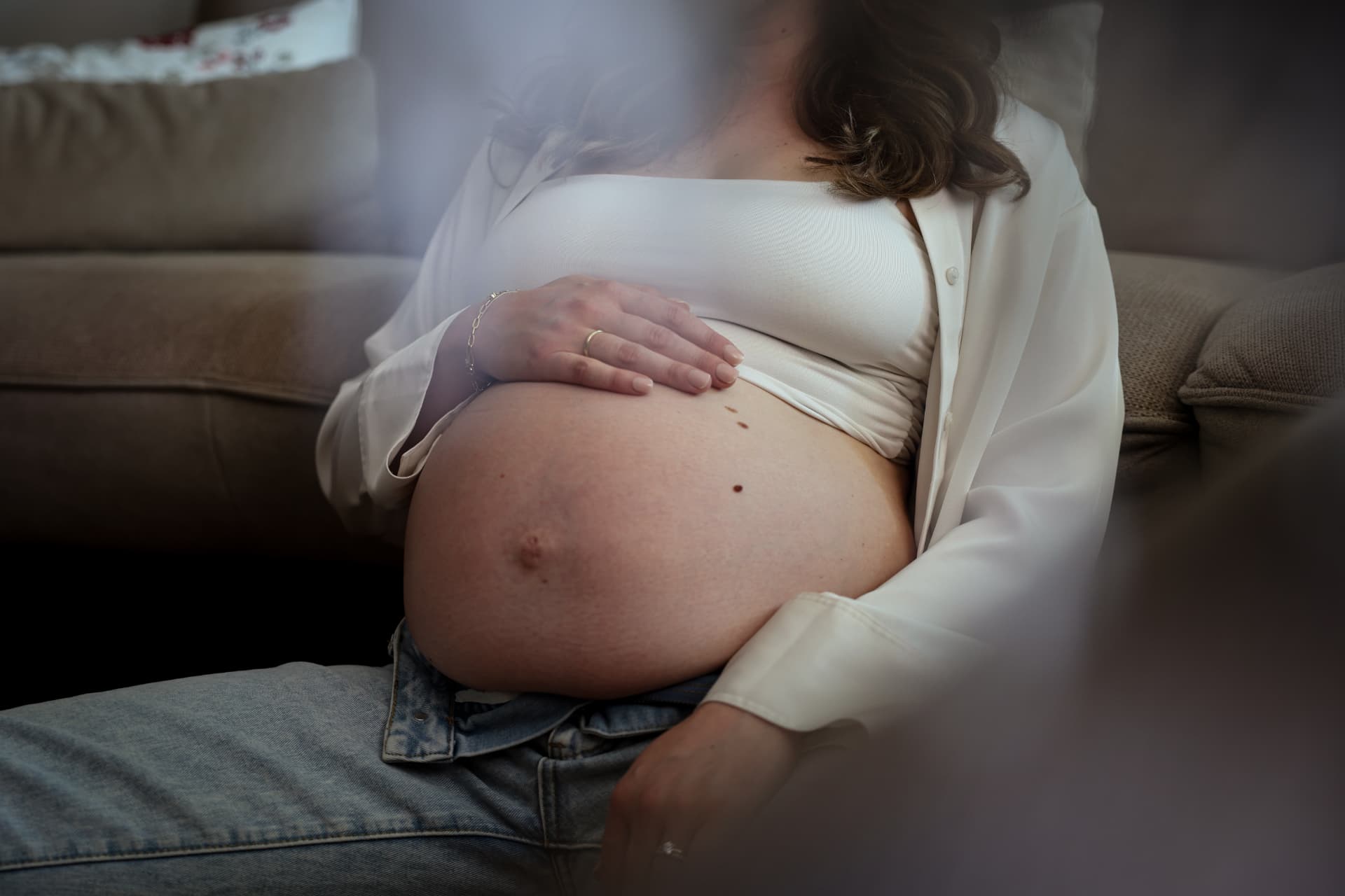 Schwangere sitzt auf einem Sofa und hält liebevoll ihren Babybauch