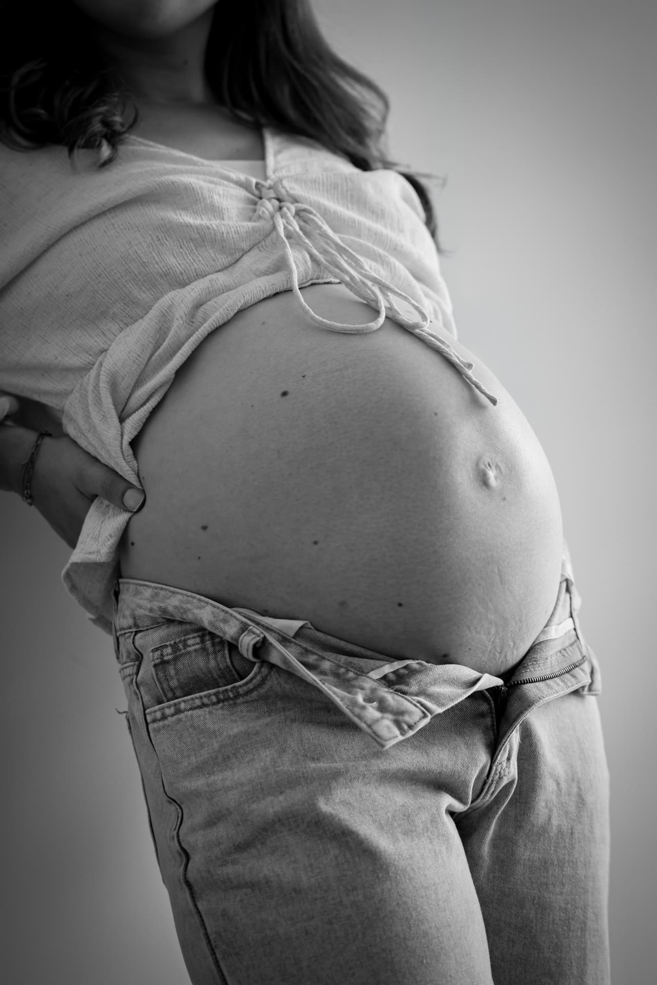 Schwarzweiß-Aufnahme eines Babybauchs mit gebundener Bluse