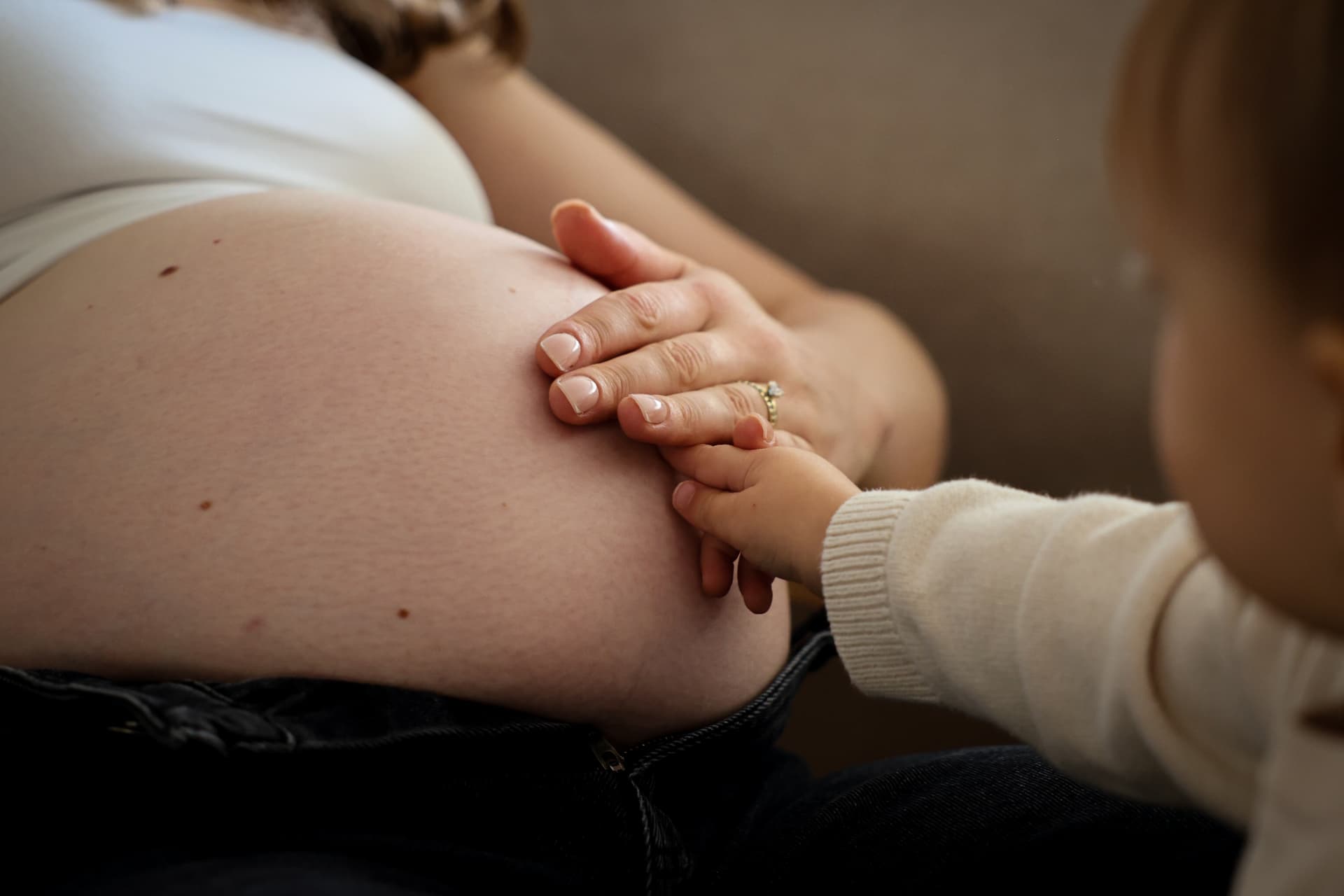 Kleine Kinderhand legt sich auf den Babybauch der Mutter