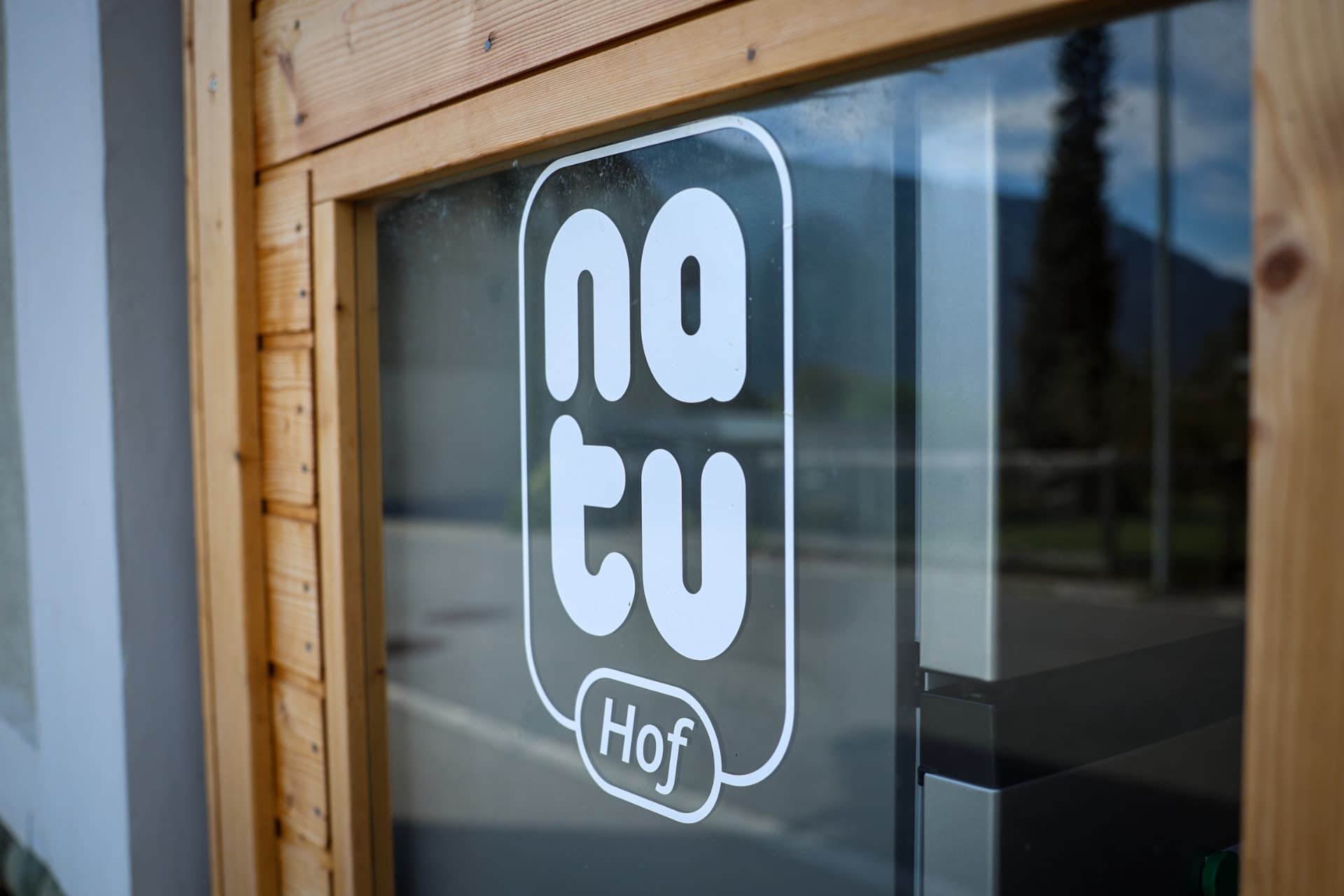Weißes Natu-Hof-Logo als Folienplot auf einer Glastür mit Holzrahmen