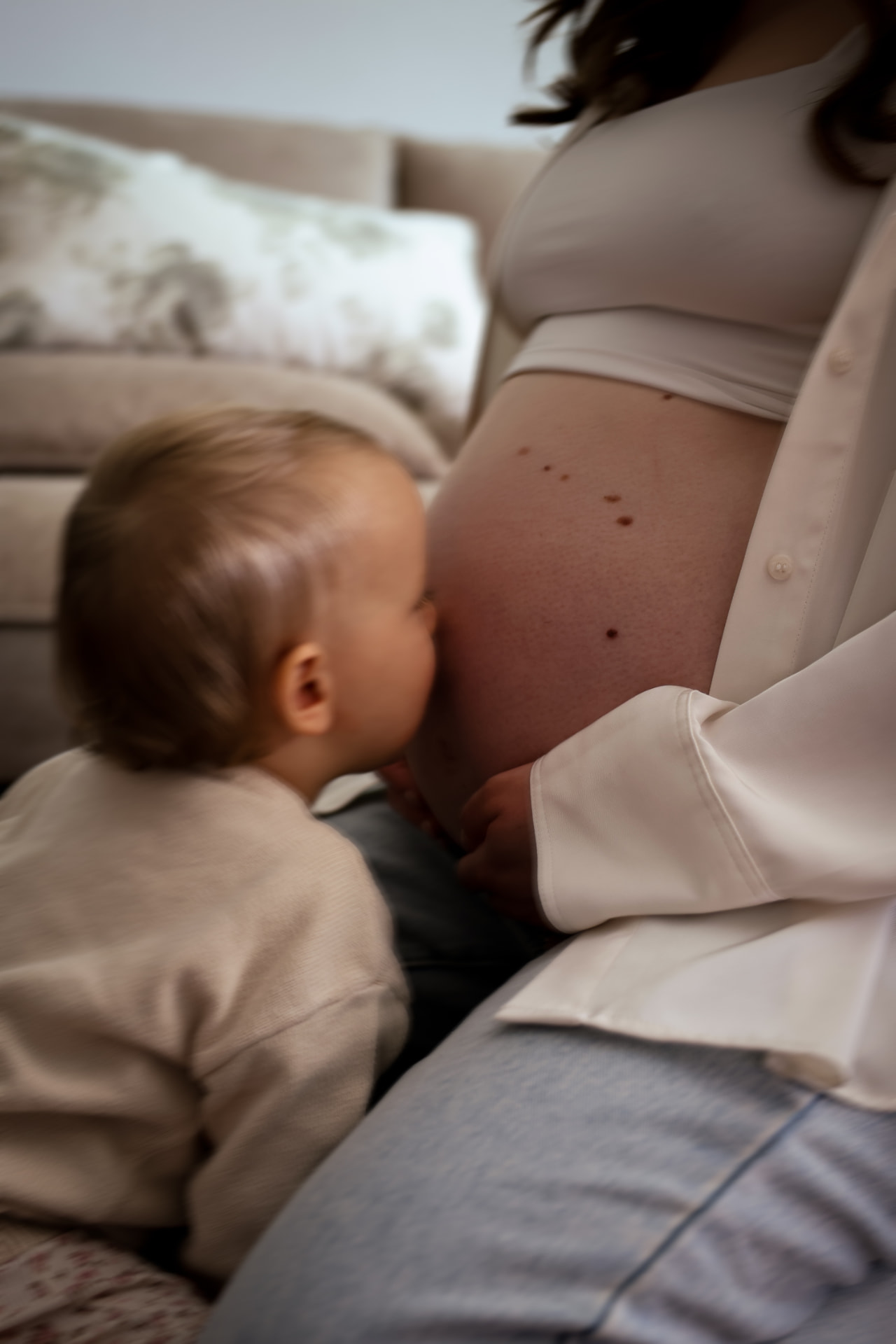 Kleinkind schmiegt sich an den Babybauch der Mutter auf dem Sofa